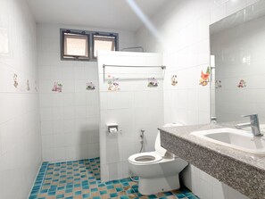A bathroom with white tiles, a toilet, a sink, and a window. - Grand Amazon Hotel by Zuzu (Lampang)