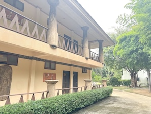 A building with a balcony, a stone pillar, and a hedge.