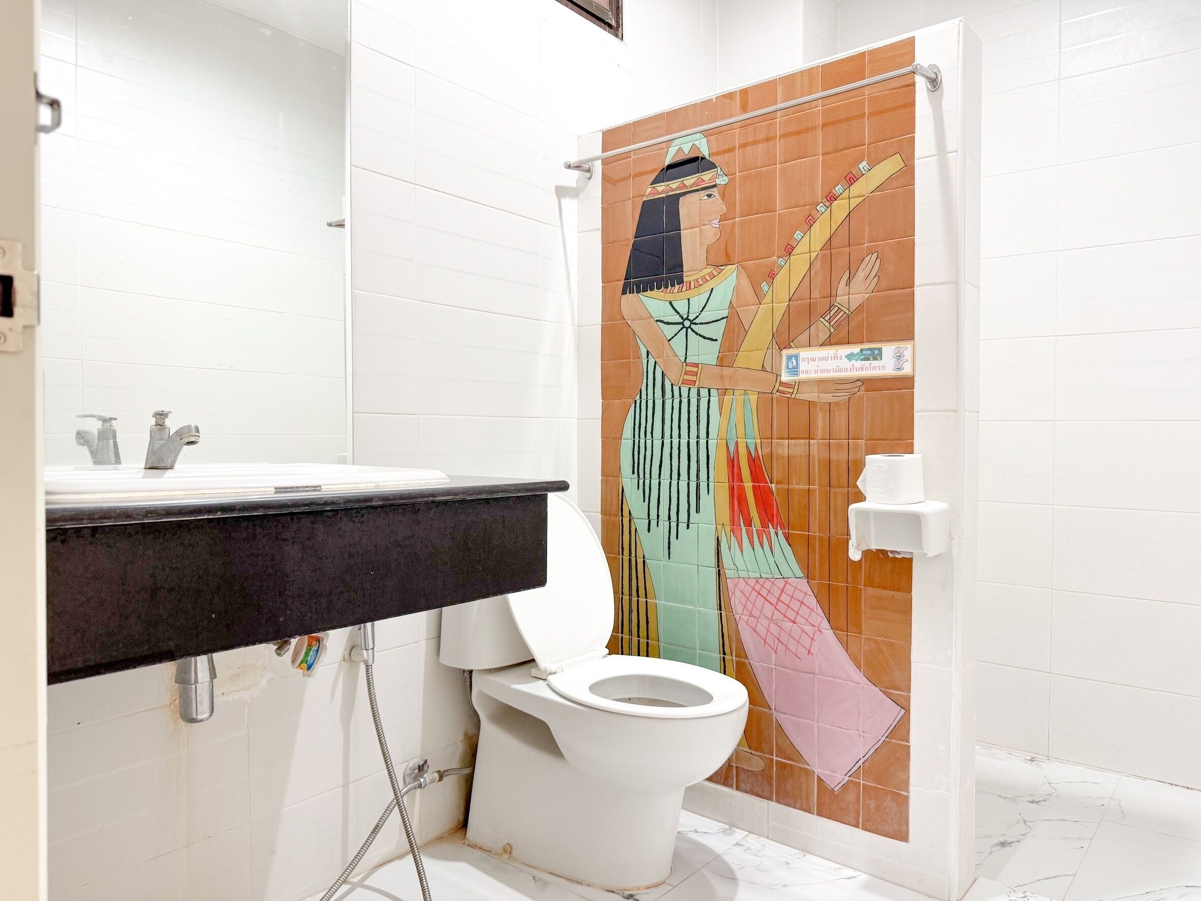 A bathroom with a white toilet, a sink with a black countertop, and a shower curtain with a colorful mural.
