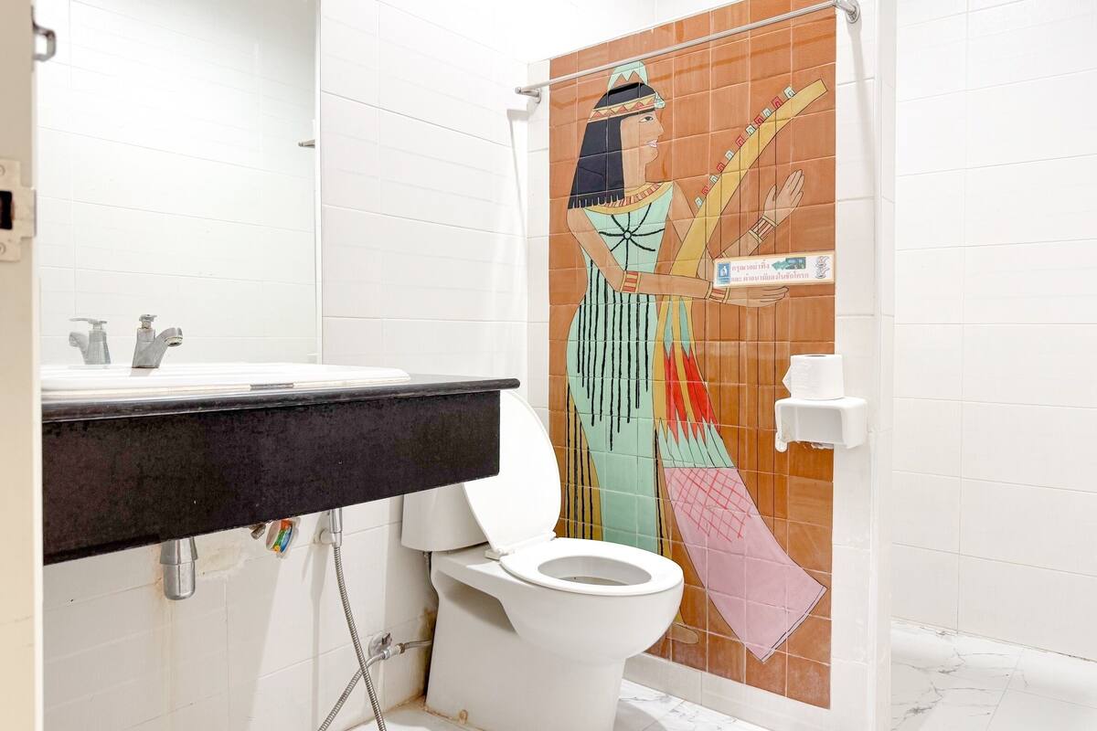 A bathroom with a white toilet, a sink with a black countertop, and a shower curtain with a colorful mural.