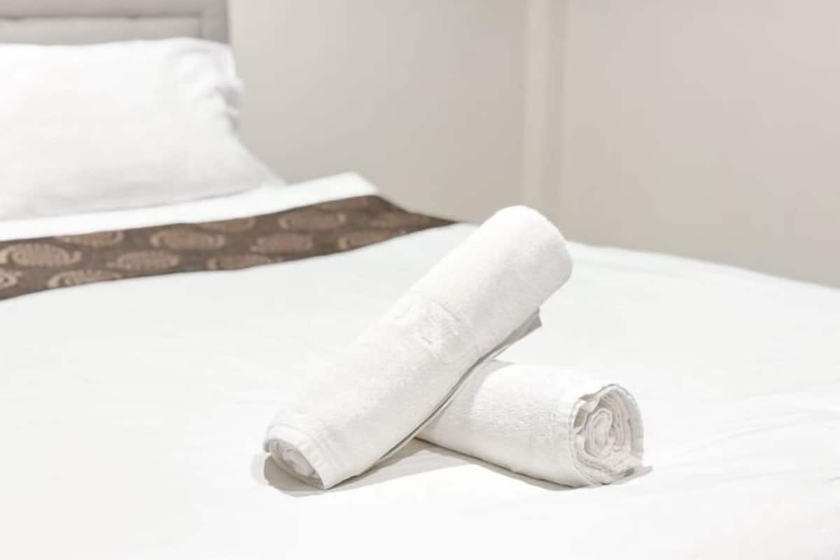 A neatly made bed with a white sheet and a rolled white towel.