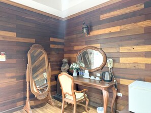 A corner room with wooden panel walls, a wooden desk with a mirror, a chair, a statue, and a white refrigerator.