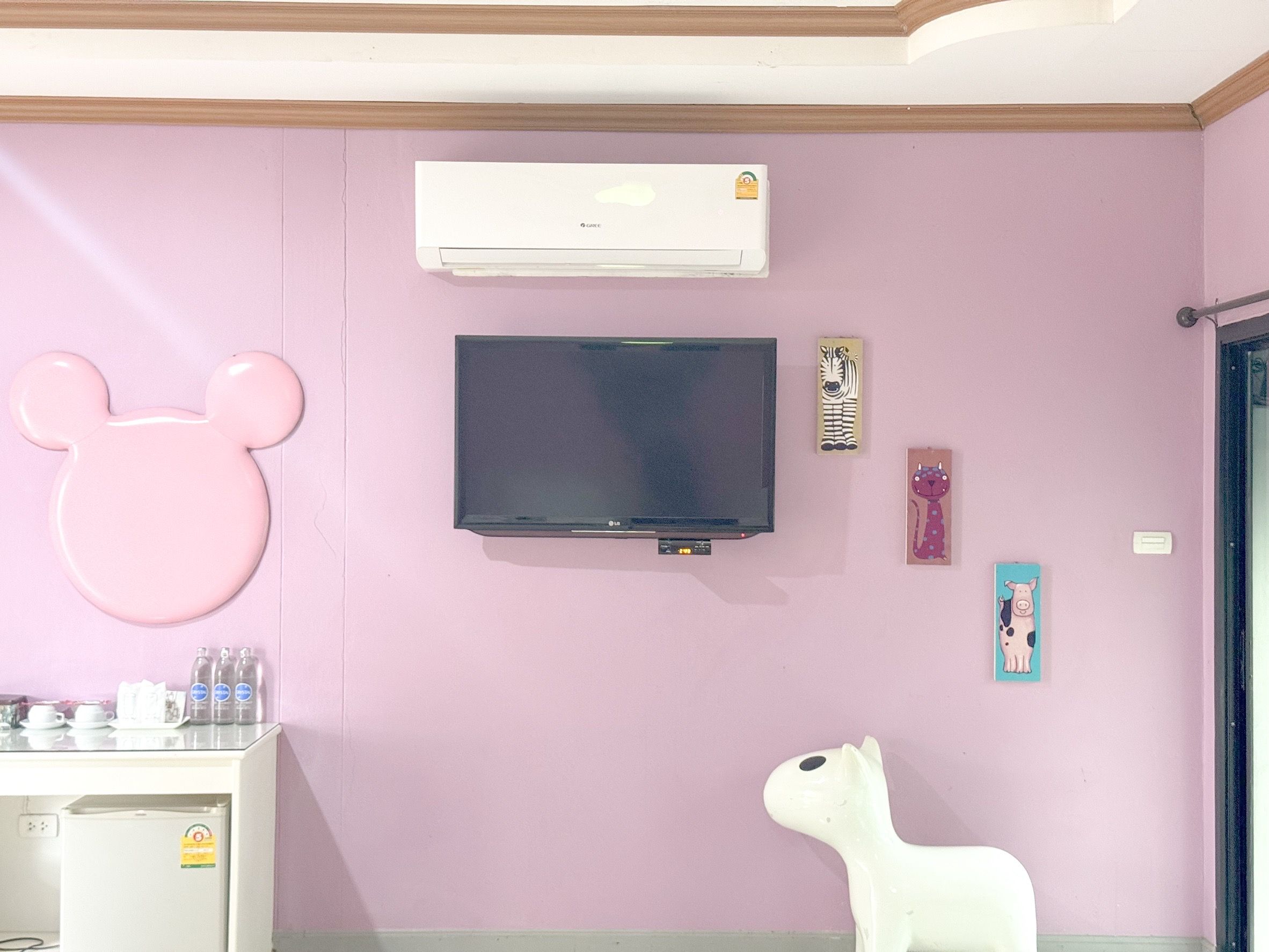 Una habitación con pared rosa, televisor montado, aire acondicionado y refrigerador blanco.