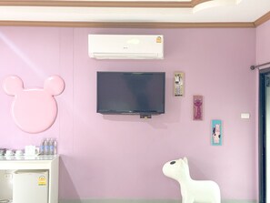 Ein Zimmer mit einer rosafarbenen Wand, einem Wand-Fernseher, einer Klimaanlage und einem weißen Kühlschrank.