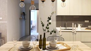 Un moderno comedor con una mesa de madera preparada para dos personas, con bombillas de vidrio transparente, un jarrón con hojas verdes y una bandeja con platos y vasos.