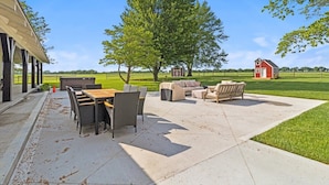An outdoor patio area with a table and chairs, a sofa, and a red building in the background.