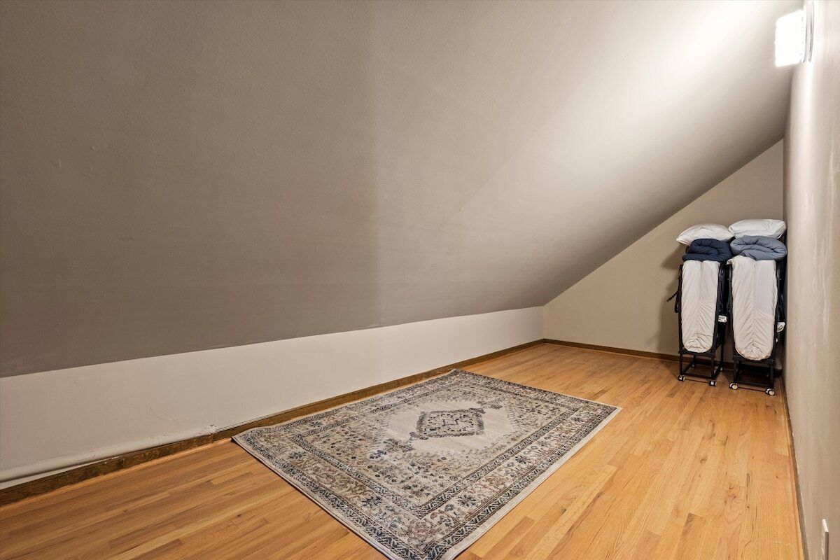 Una stanza con pavimento in legno, un tappeto decorato, un angolo con parete bianca e un porta asciugamani con asciugamani piegati.