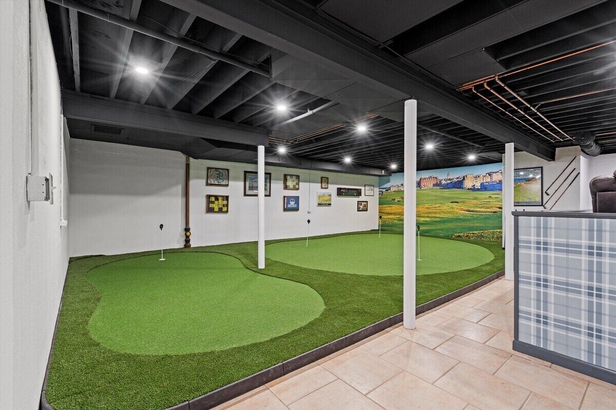 An indoor golf simulation area with artificial turf, wall-mounted scoreboards, and a mural of a golf course.