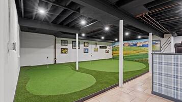 An indoor golf simulation area with artificial turf, wall-mounted scoreboards, and a mural of a golf course.