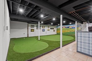 An indoor golf simulation area with artificial turf, wall-mounted scoreboards, and a mural of a golf course. - Landing(43M0)- Sleeps 20 + Airway Strip + Hot Tub (Pleasant Hill)
