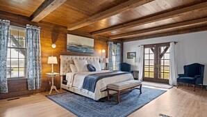 A bedroom with a large bed, a wooden ceiling, and a view through a glass door.