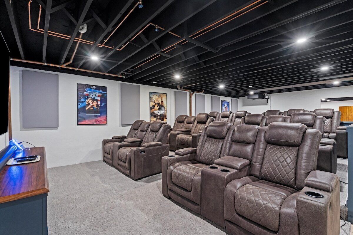 A home theater with multiple reclining leather chairs, a wooden desk, and posters on the wall.