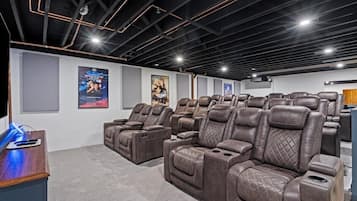 A home theater with multiple reclining leather chairs, a wooden desk, and posters on the wall.