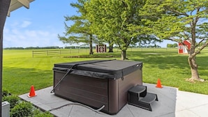 A hot tub outdoors with a tree and a red building in the background. - Landing(43M0)- Sleeps 20 + Airway Strip + Hot Tub (Pleasant Hill)