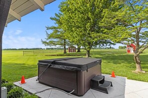 A hot tub outdoors with a tree and a red building in the background. - Landing(43M0)- Sleeps 20 + Airway Strip + Hot Tub (Pleasant Hill)