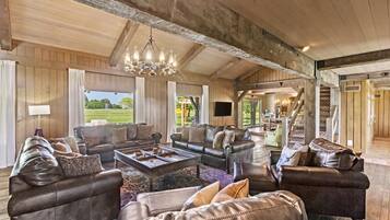 A spacious living room with leather sofas, a chandelier, and a large window offering a view of the outdoors.