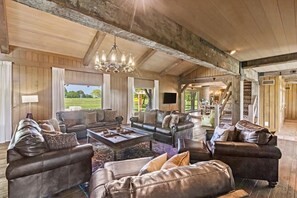 A spacious living room with leather sofas, a chandelier, and a large window offering a view of the outdoors. - Landing(43M0)- Sleeps 20 + Airway Strip + Hot Tub (Pleasant Hill)