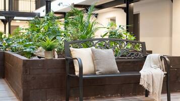 A bench with cushions, surrounded by greenery and a wooden planter.