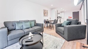 A modern living room with two grey sofas, a small black coffee table, and a dining area in the background.