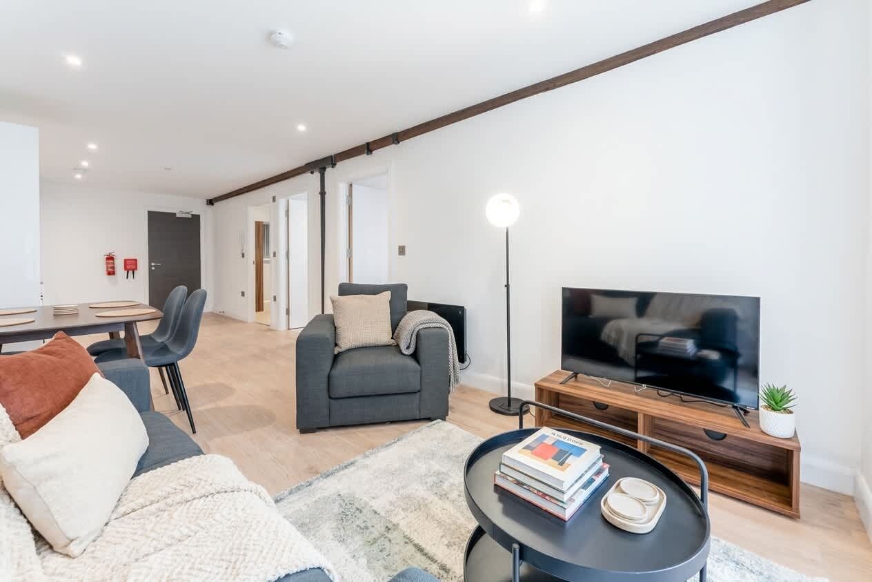 A modern living room with a sofa, a coffee table, a TV, and a dining area with chairs and a table.