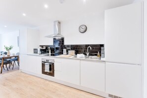 A modern kitchen with white cabinetry, a stainless steel range hood, and a black tiled backsplash. - Spacious & Bright 2 Bed Burton-on-Trent Apartment (Burton upon Trent)