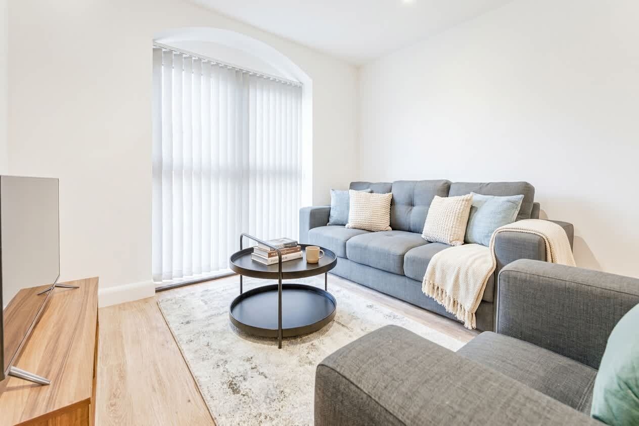 Een moderne woonkamer met een grijze bank, een ronde salontafel en een televisie op een houten dressoir.