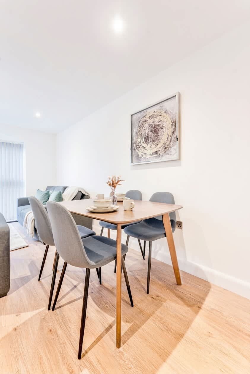 A modern dining area with a round table, four chairs, and a minimalist abstract painting on the wall.