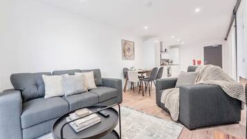 A modern living room with a grey sofa, a coffee table, and a dining area in the background.