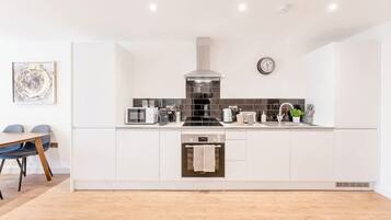 A modern kitchen with white cabinetry, a stainless steel range hood, a built-in oven, and a dining area with a table and chairs.