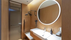 A modern bathroom with a glass shower enclosure, a large mirror, and a white sink with a soap dispenser.