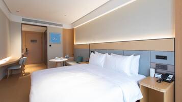A hotel room with a large bed, bedside table with a phone, a small desk with a chair, and a round table with a chair.