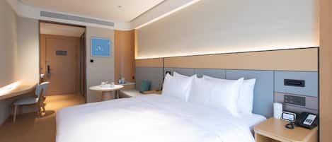 Una habitación de hotel con una cama grande, una mesita de noche con teléfono, un escritorio pequeño con silla y una mesa redonda con otra silla.