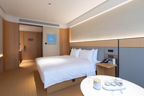 A modern hotel room with a neatly made bed, a bedside table with a phone and a small lamp, and a round table with a tray of breakfast items. - Ji Hotel Wuhan Hannan Xingcheng Avenue (Wuhan)