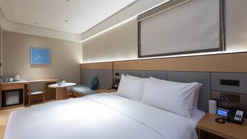 A hotel room with a large bed, bedside table with a phone, a desk with a chair, and a small table with a chair.