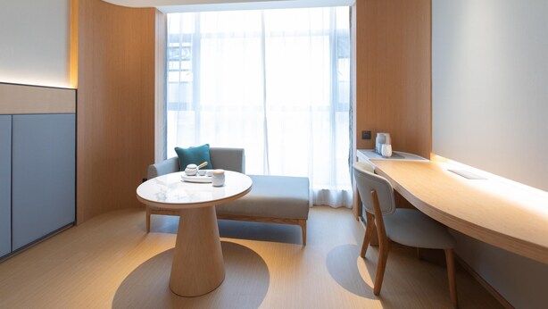 A modern hotel room with a round table, a sofa, and a desk.