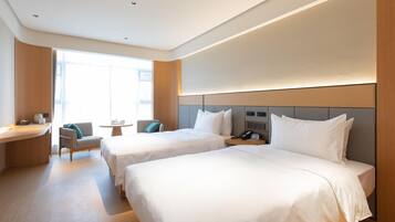 A hotel room with two beds, a desk, a chair, a small table, and a phone on the nightstand.