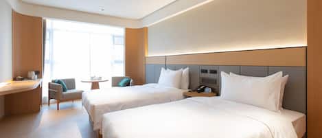 Habitación de hotel con dos camas, un escritorio, una silla, una mesita y una ventana.