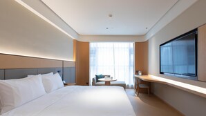 A modern hotel room with a large bed, a desk, a chair, and a TV mounted on the wall.