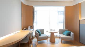 Quarto de hotel moderno com escrivaninha de madeira, dois poltronas, uma mesa redonda e uma cama.