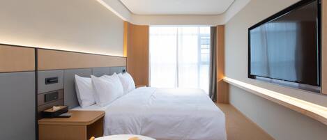 Una habitación de hotel moderna con una cama grande, mesitas de noche, un televisor de pantalla plana y un ventanal con cortinas.