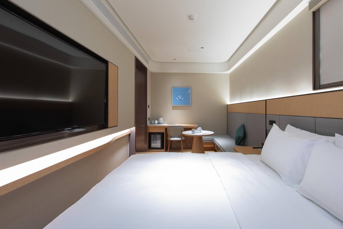 A modern hotel room with a large bed, a desk, a chair, and a small table.