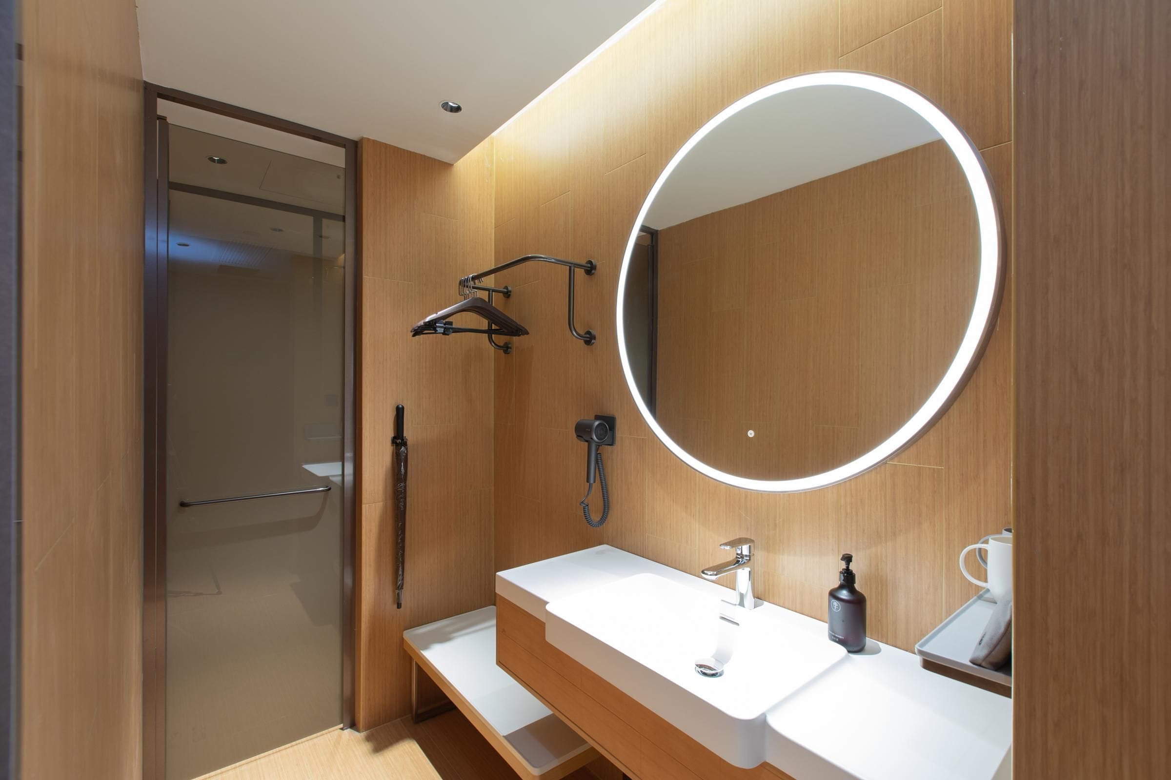 A modern bathroom with a wooden vanity, a large mirror, and a shower area.