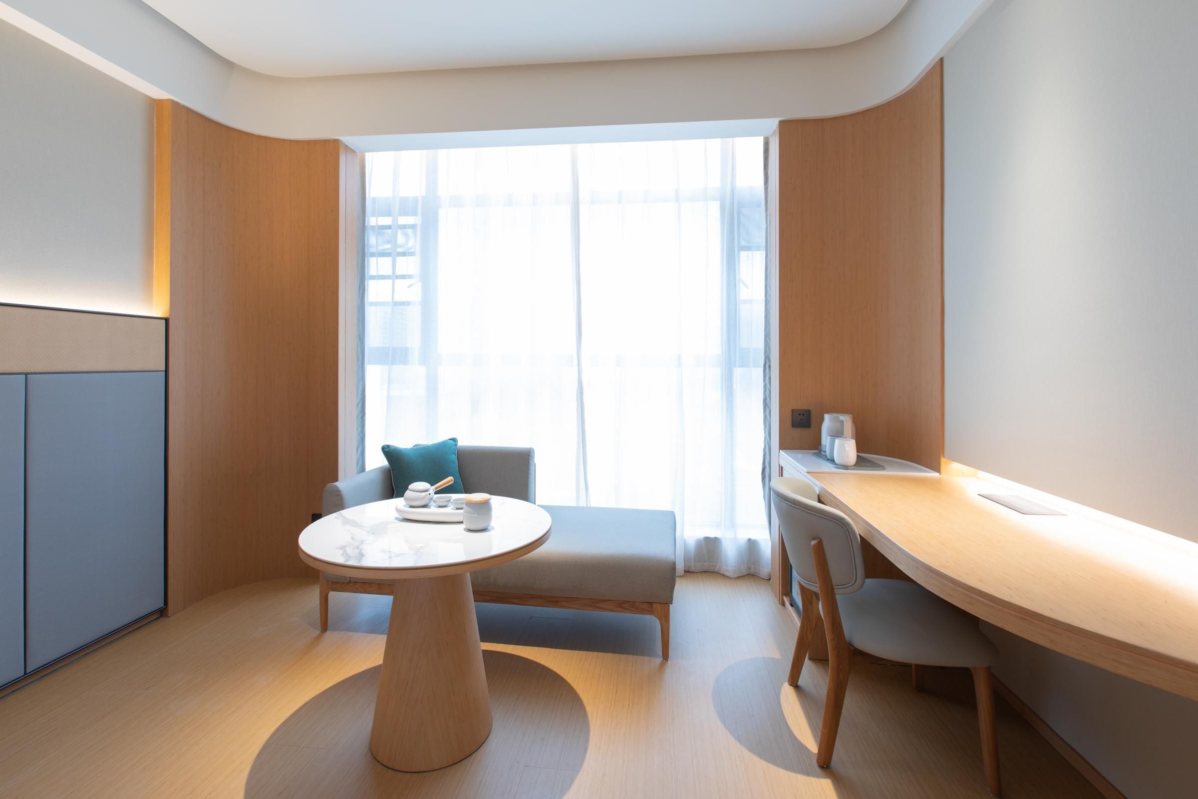 Ein modernes Hotelzimmer mit rundem Tisch, einer Couch und einem Schreibtisch.