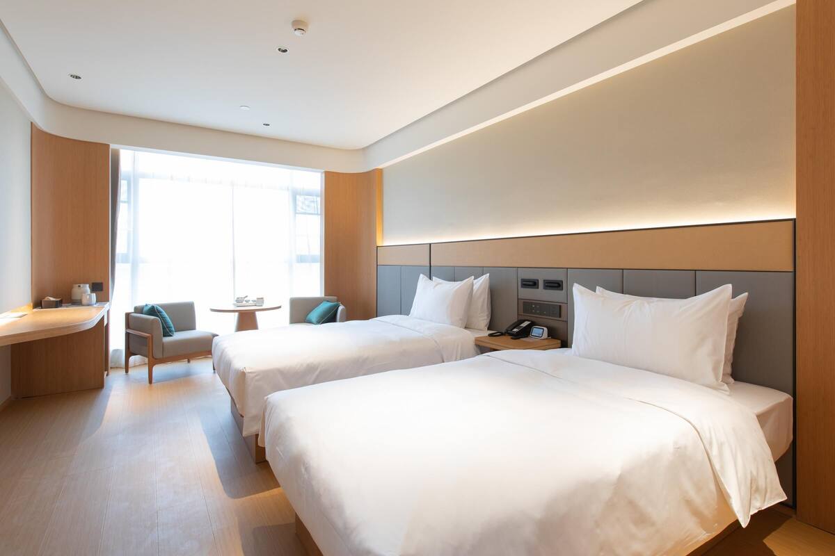 A hotel room with two beds, a desk, a chair, a small table, and a phone on the nightstand.