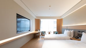 A hotel room with two beds, a desk, a chair, and a small table.