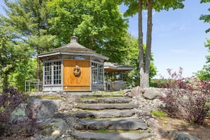 A wooden gazebo with a circular roof, surrounded by a stone pathway and lush greenery. - Badger's Sett - Estate on point with hot tub (Battersea)