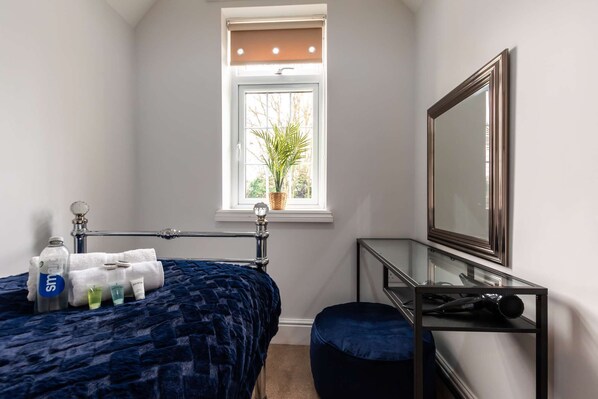 Une chambre à coucher avec un lit, une fenêtre ornée d’une plante, un miroir et une table de chevet avec des articles de toilette.