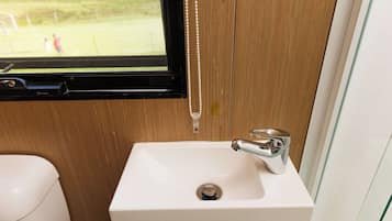 Une salle de bain avec un lavabo blanc, un robinet chromé et une fenêtre donnant sur un champ verdoyant.