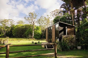 Un bâtiment moderne, de plain-pied, doté d’une terrasse en bois et entouré d’une végétation luxuriante et d’arbres.