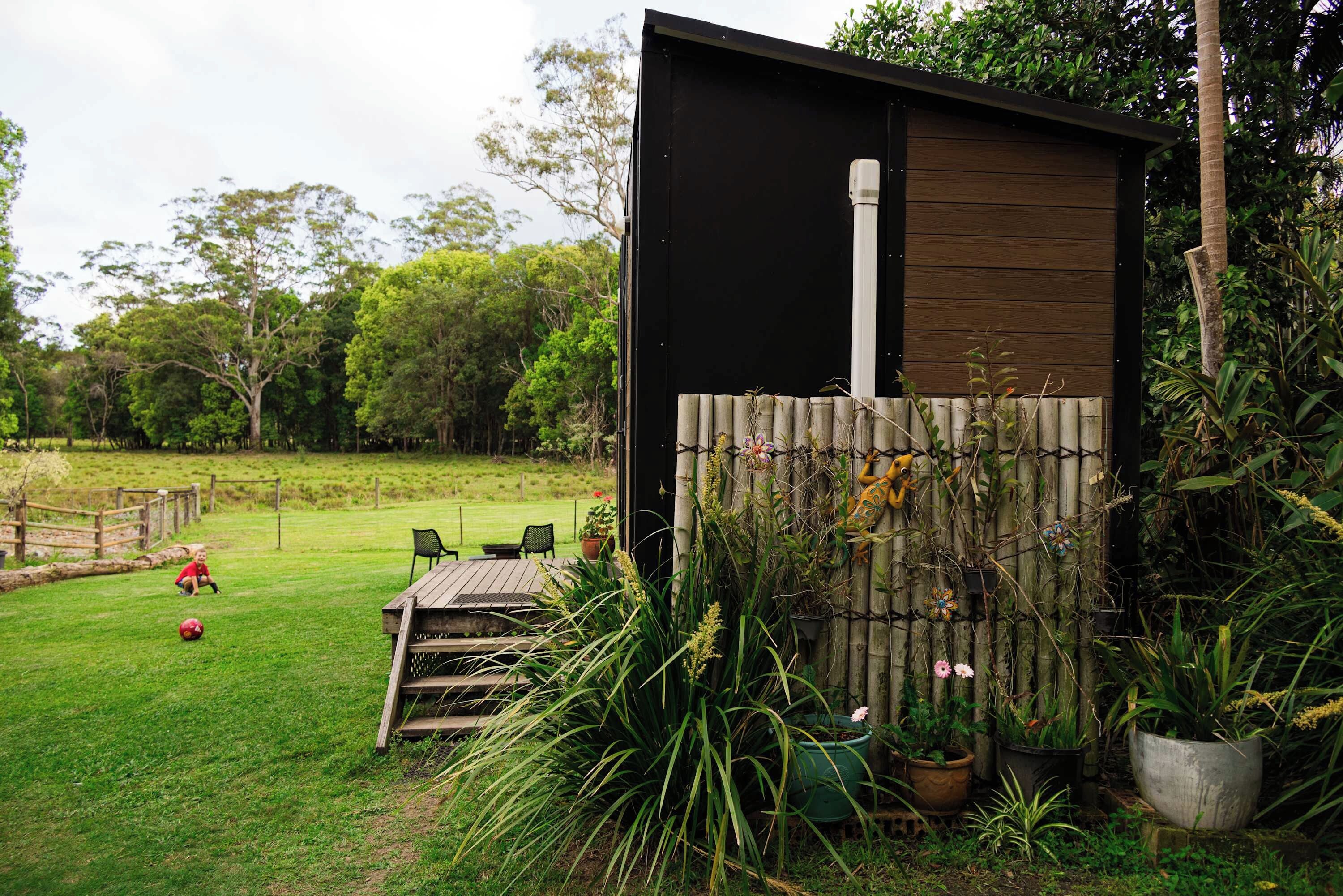 Une structure en bois à l’extérieur noir, entourée d’une clôture en bambou, et une zone herbeuse avec une table et des chaises.